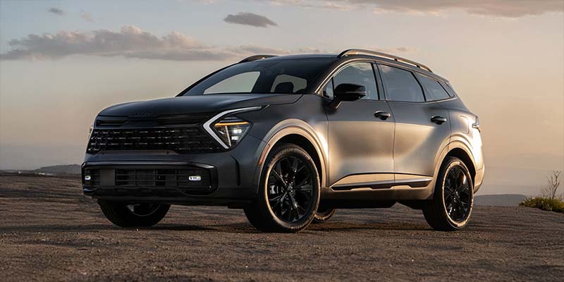 Matte black 2026 Kia Sportage Hybrid SUV parked on a scenic overlook during sunset.
