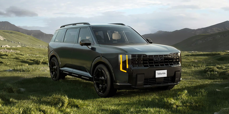 Dark green 2027 Kia Telluride SUV parked on a grassy field with mountains in the background.